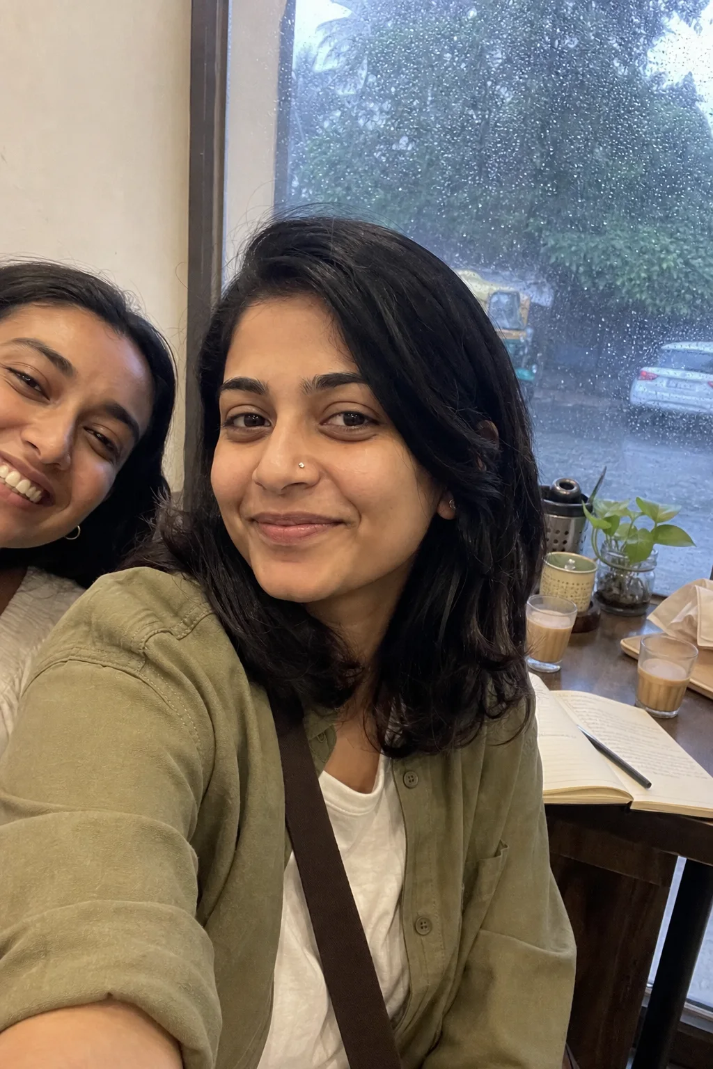 Meera taking a café selfie with a friend on a rainy afternoon